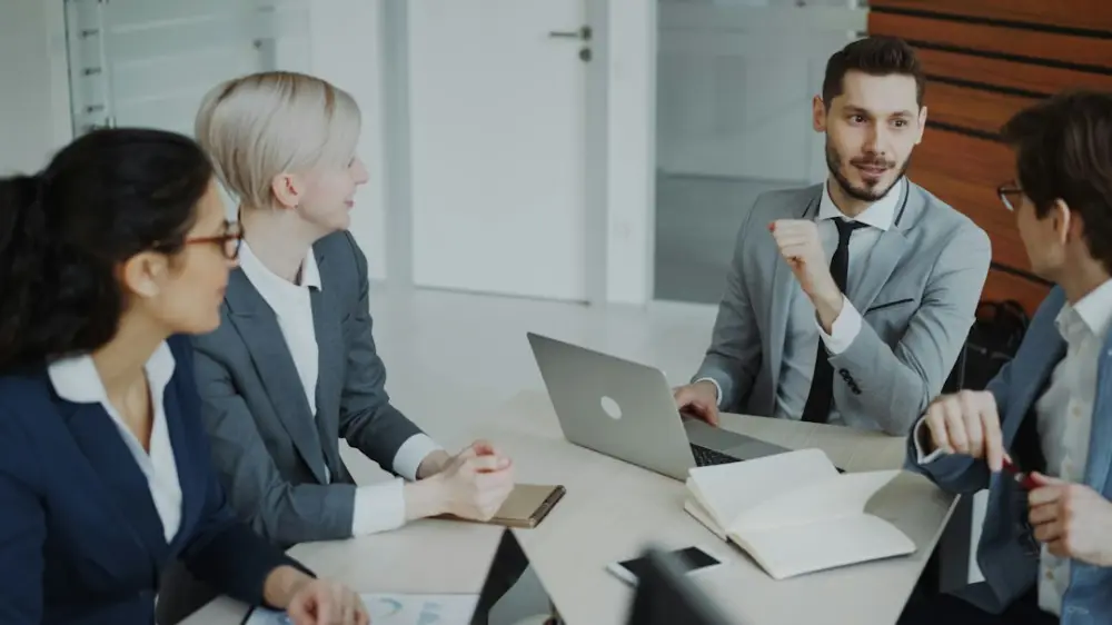 Four professionals in a business meeting around a table, illustrating evaluating public-policy implementation structures